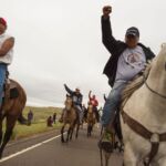 Native Americans ride with raised fists to a sacred burial ground that was disturbed by bulldozers building the Dakota Access Pipeline (DAPL), near the encampment where hundreds of people have gathered to join the Standing Rock Sioux Tribe's protest of the oil pipeline slated to cross the nearby Missouri River, September 4, 2016 near Cannon Ball, North Dakota.  
Protestors were attacked by dogs and sprayed with an eye and respiratory irritant yesterday when they arrived at the site to protest after learning of the bulldozing work. / AFP / ROBYN BECK        (Photo credit should read ROBYN BECK/AFP via Getty Images)
